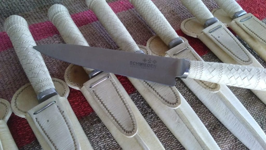 Several Schmieden Gaucho knives with braded leather handles, some in leather sheaths.
