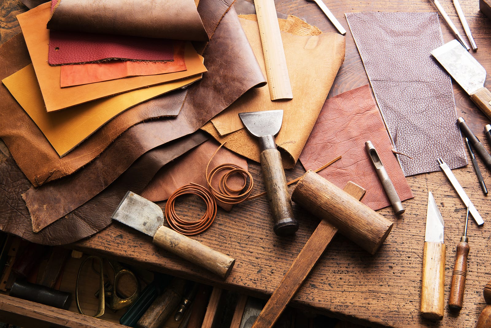 wooden table with leather scraps, crafting tools, and materials used for traditional leatherworking.