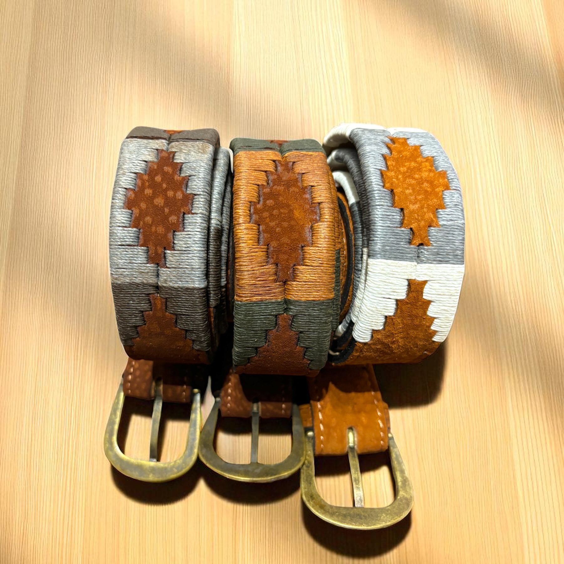 Group of three Capybara belts with hand-embroidered patterns in grey, pearl grey, and rust brown with hunter green