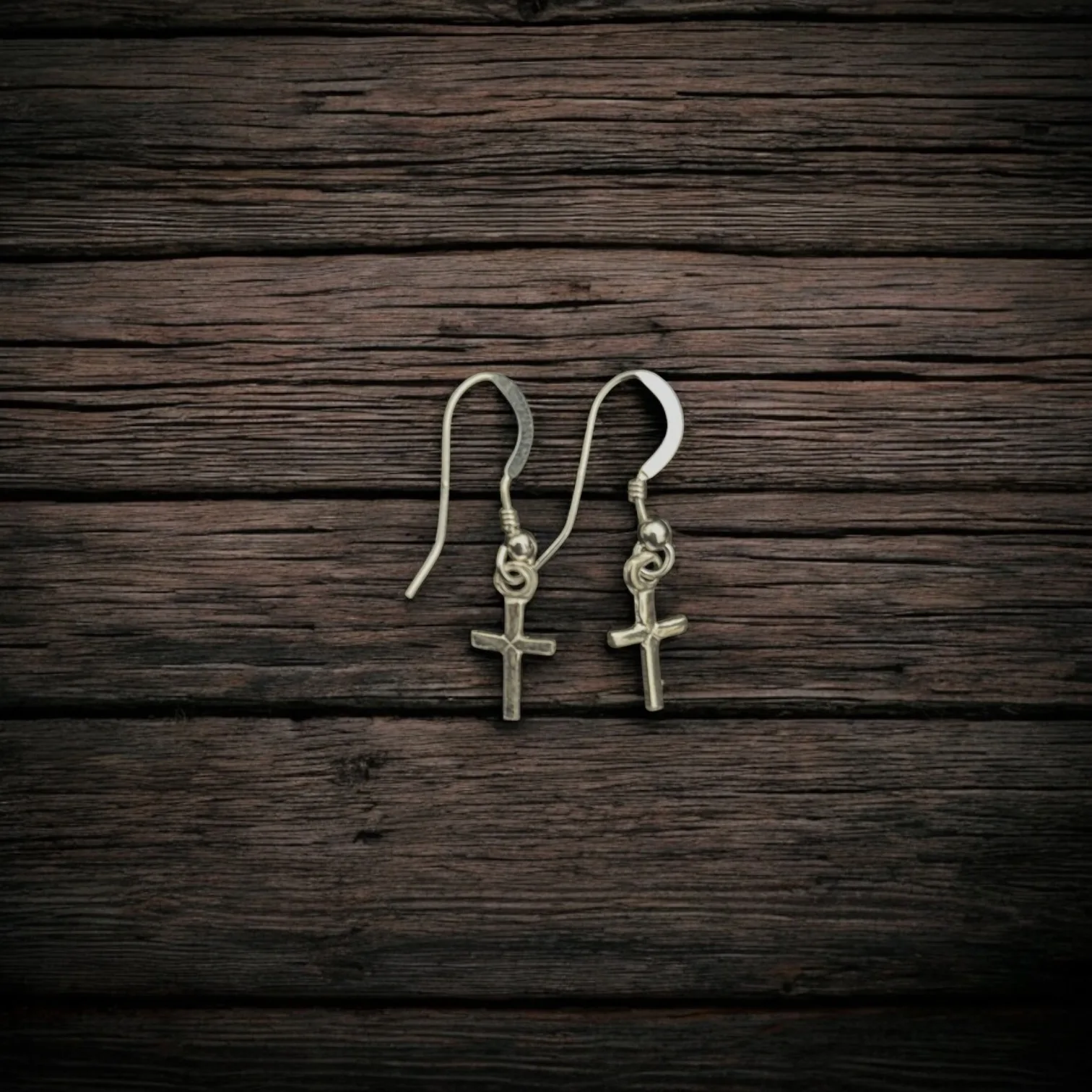 925 silver cross earrings resting on rustic wooden surface