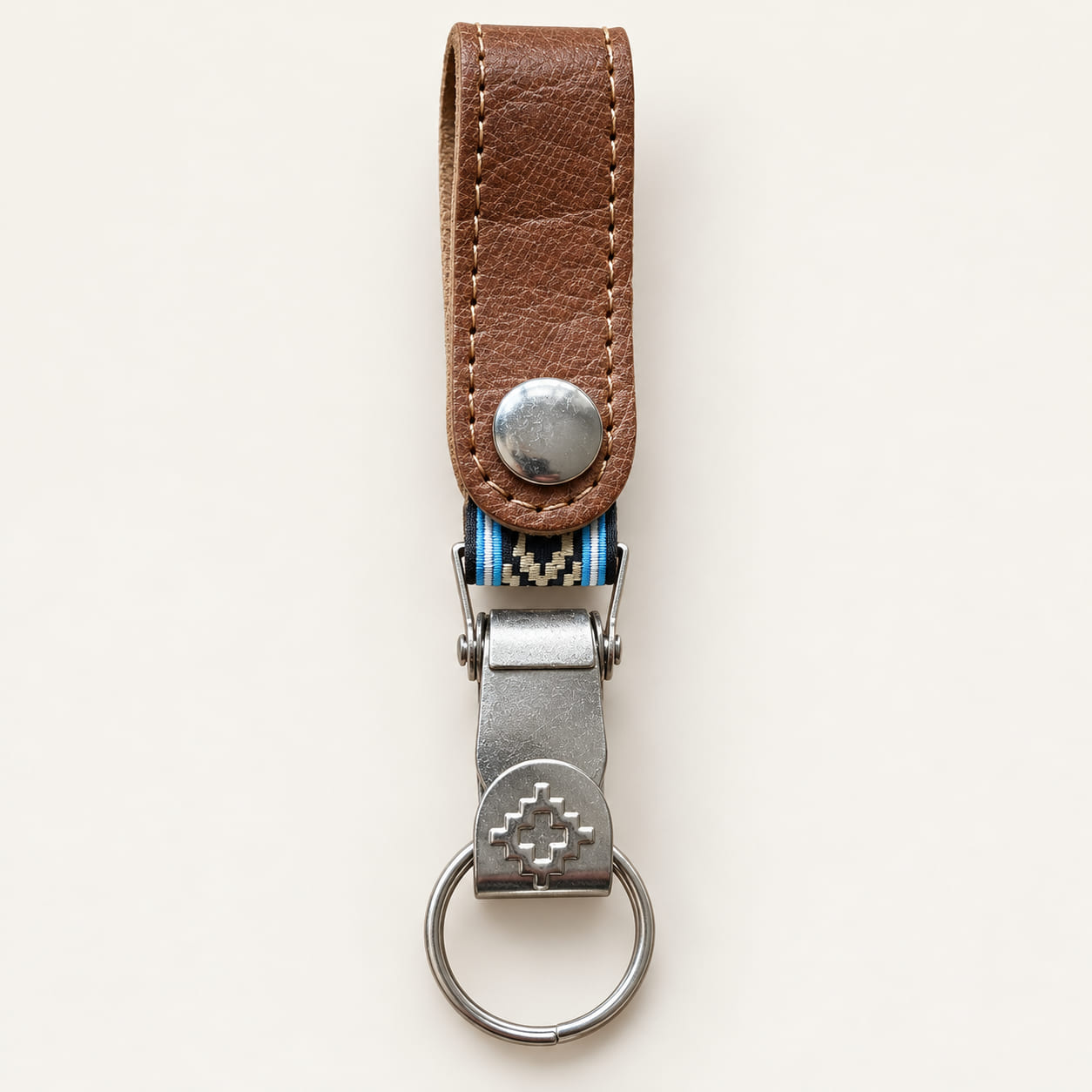 Brown leather belt clip keychain with geometric Guarda Pampa metal motif and woven band edged in sky blue and white.