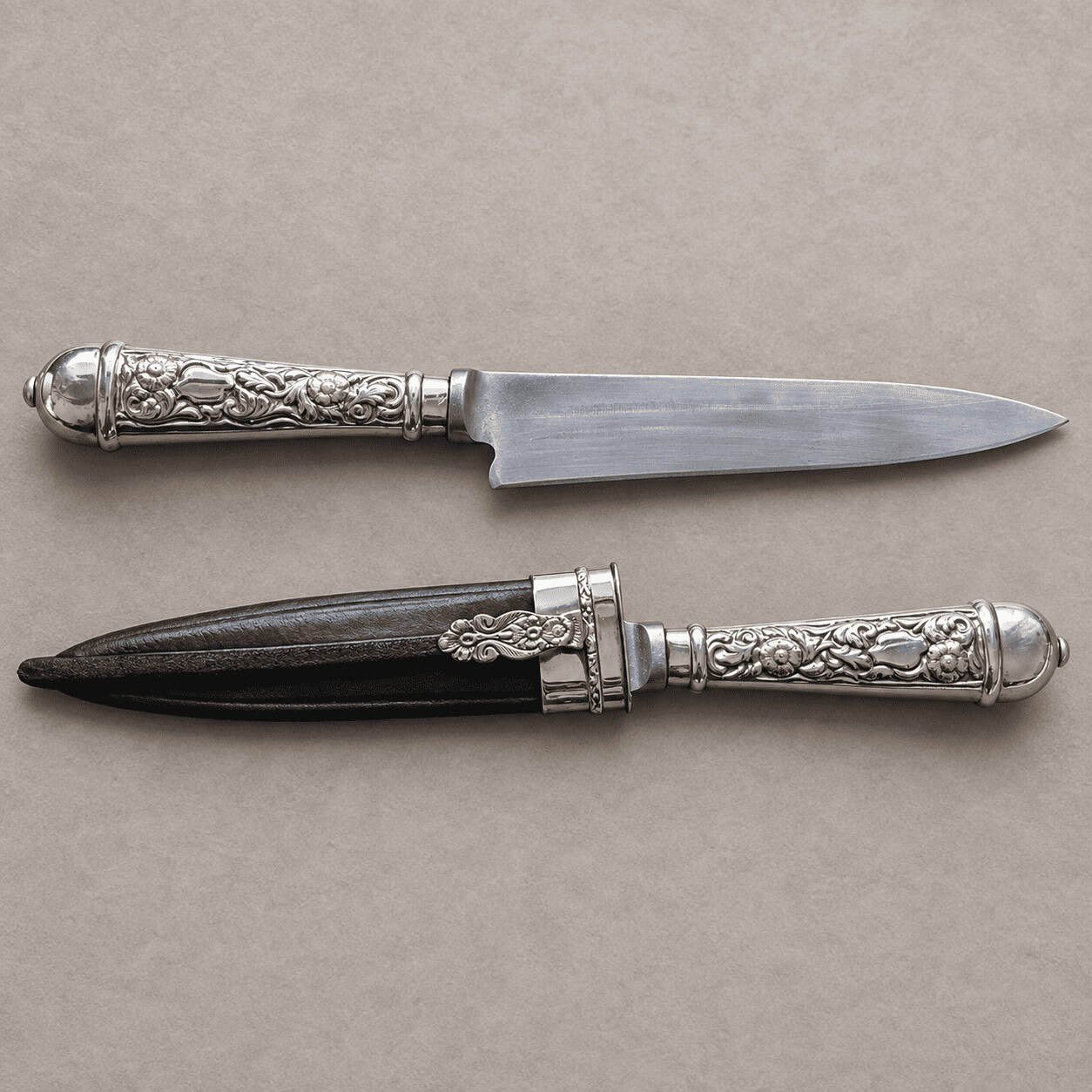 Two Argentine gaucho knives with engraved alpaca handles, one showing its blade and the other in a black leather sheath