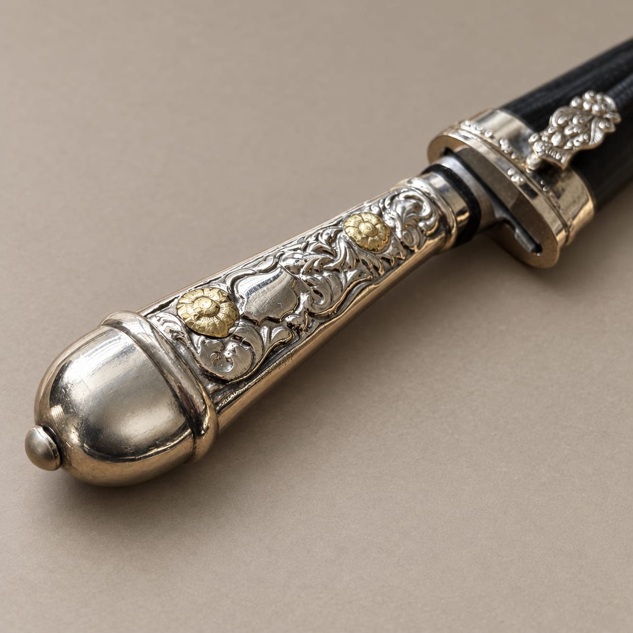 Close-up of an Argentine gaucho knife handle with floral engraving, two gold-toned accents, and a rounded pommel