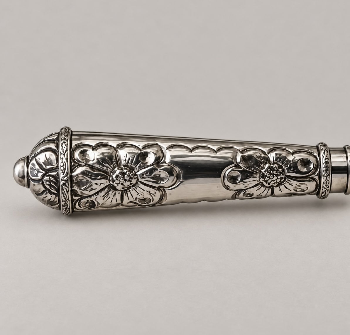 Close-up of an Argentine knife handle in silver-toned alpaca with two engraved floral motifs.