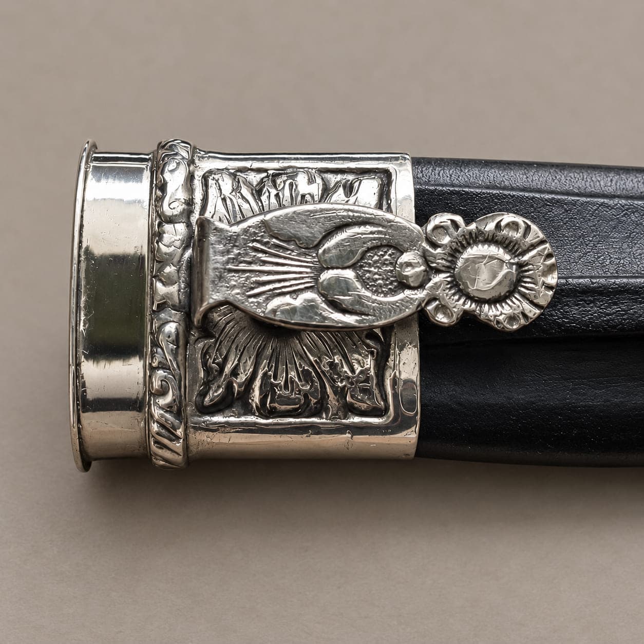 Close-up of the engraved alpaca fitting and decorative tab on a black Argentine knife sheath