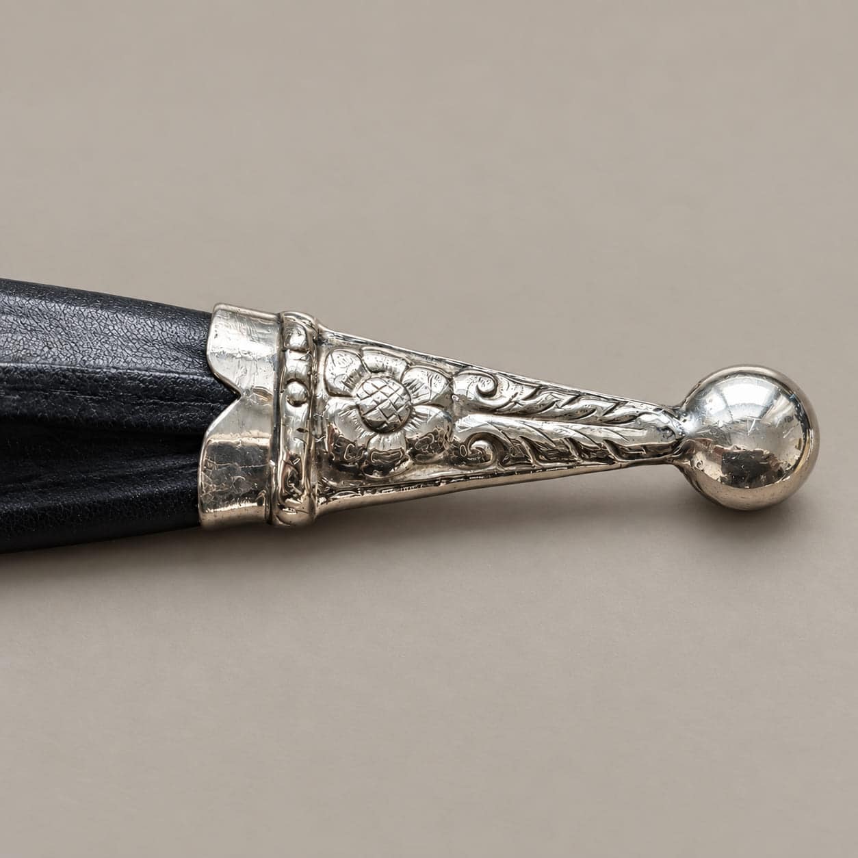 Close-up of a black knife sheath with a floral engraved alpaca tip and round finial