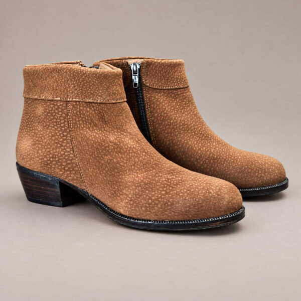 Tan capybara leather ankle boots with rounded toes, low dark heels and side zip closures, photographed on a grey-beige background. Descripción: