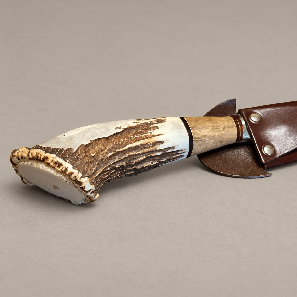Close-up of a sheathed gaucho knife showing its curved staghorn handle, natural antler base, hardwood section and riveted brown leather sheath.