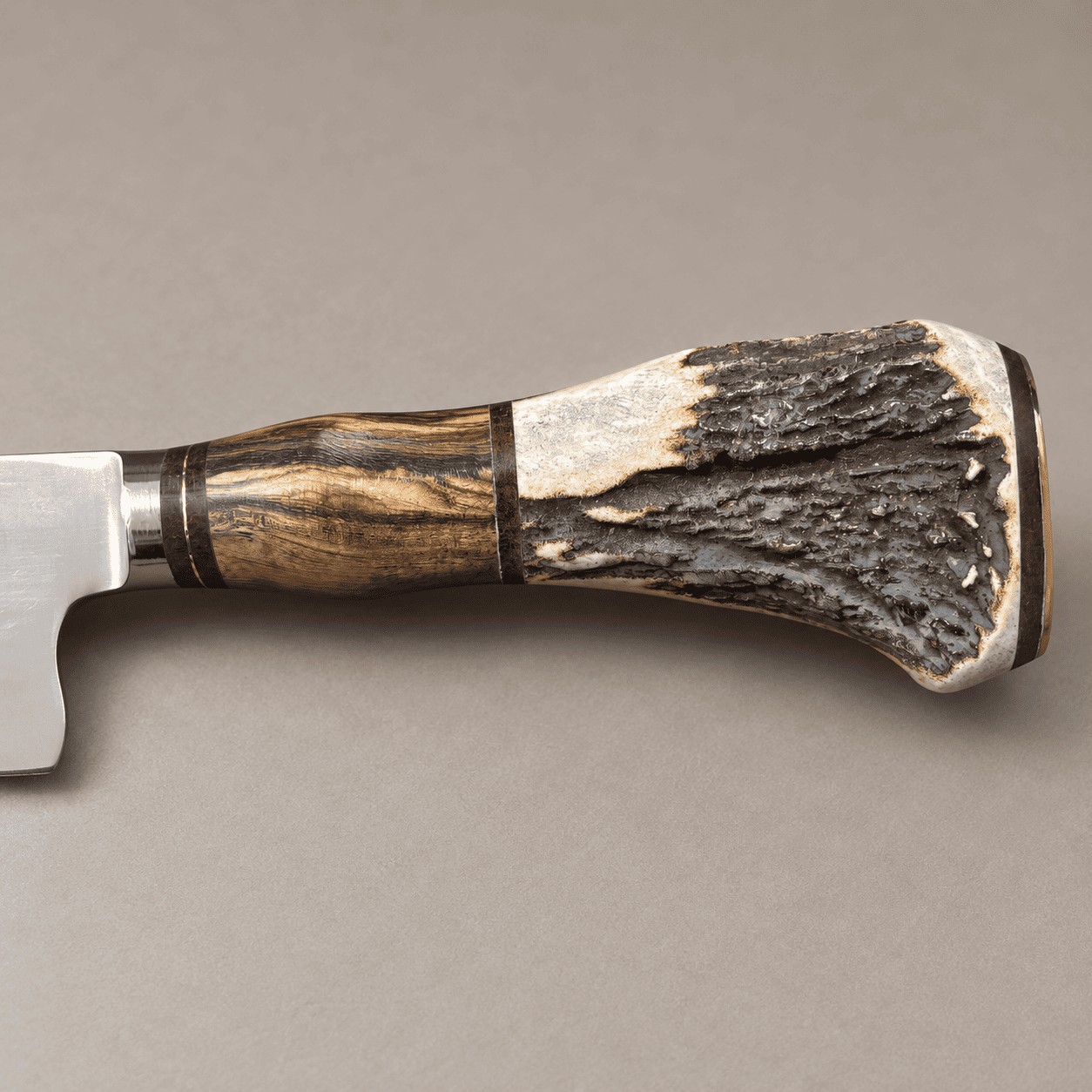 Side view of a gaucho knife handle combining golden-brown hardwood, dark textured staghorn, ivory antler and narrow spacers.