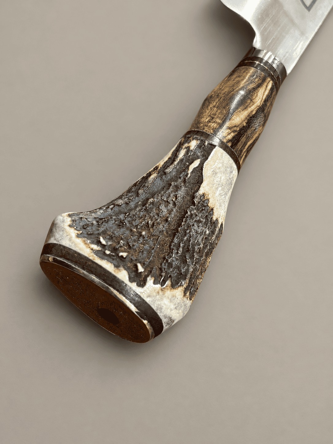 Angled close-up of a gaucho knife handle showing textured staghorn, polished hardwood and its rounded end cap.