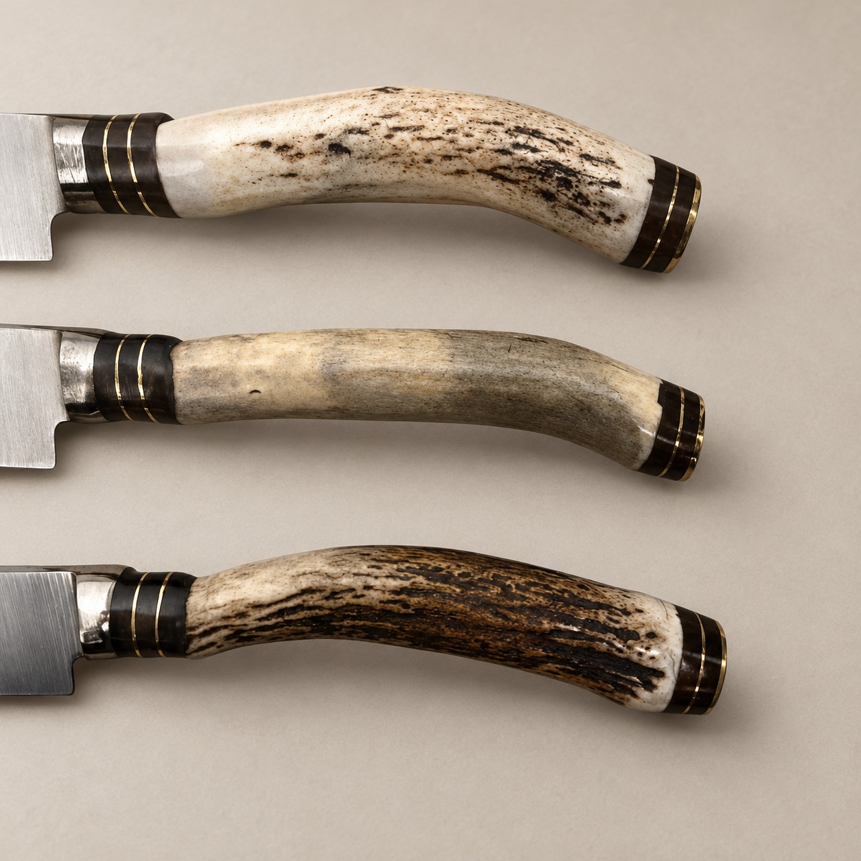Close-up of three natural staghorn handles with dark metal and brass fittings on handmade Argentine gaucho steak knives.