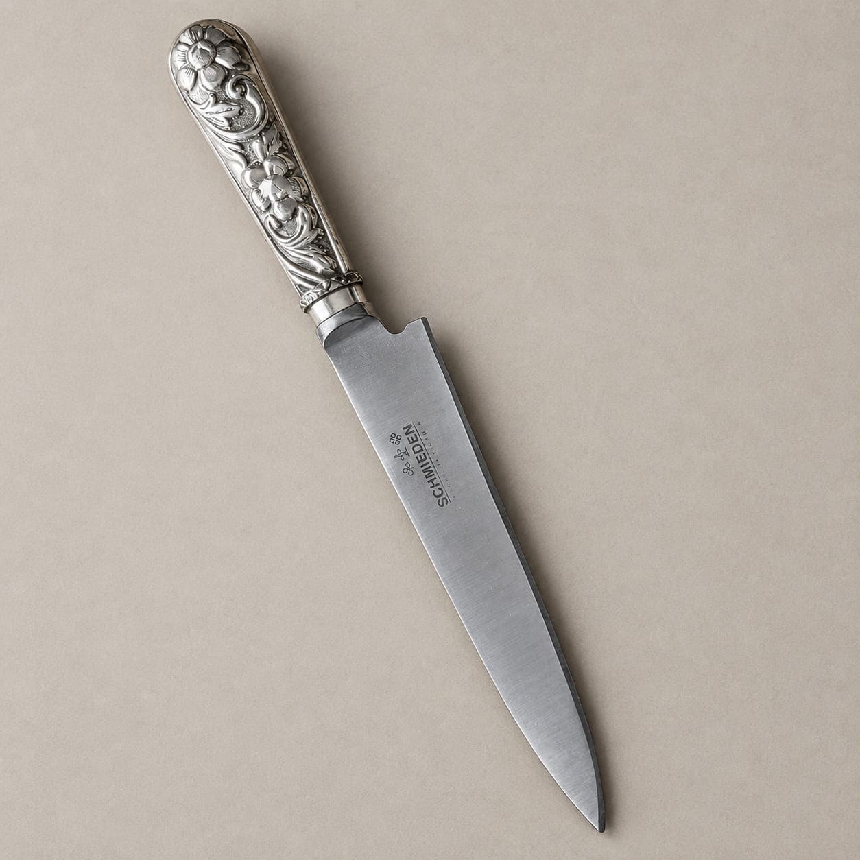 Unsheathed Schmieden knife with a pointed steel blade and a floral-engraved alpaca handle.