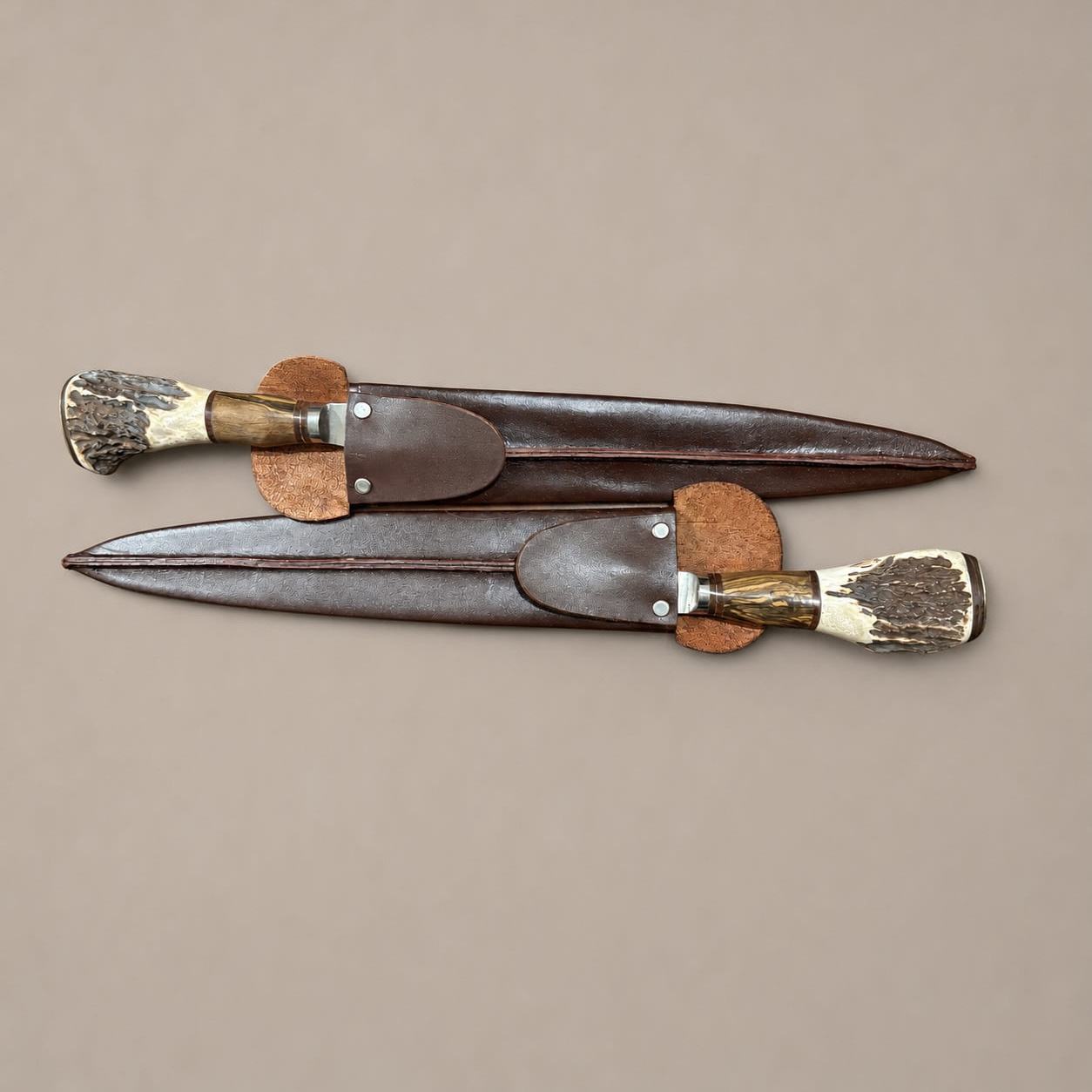 Two staghorn and hardwood gaucho knives in chocolate leather sheaths, arranged vertically in opposite directions.