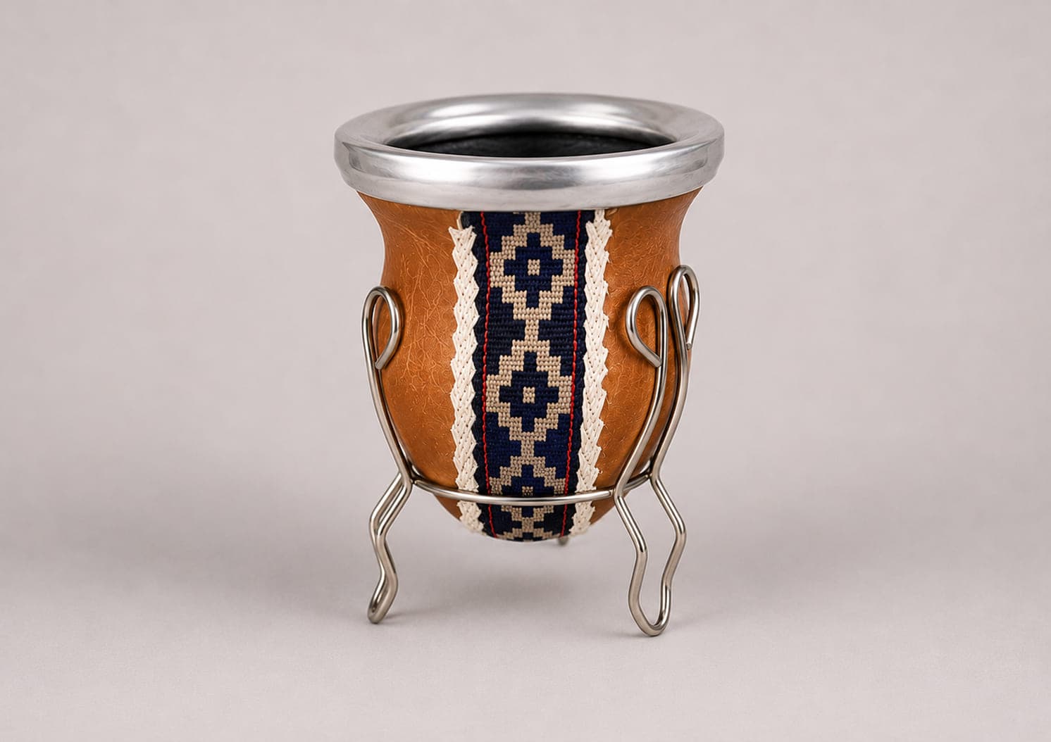 Traditional Argentine mate gourd handcrafted in genuine tan leather with an alpaca silver rim, Guarda Pampa ribbon and matching metal stand.