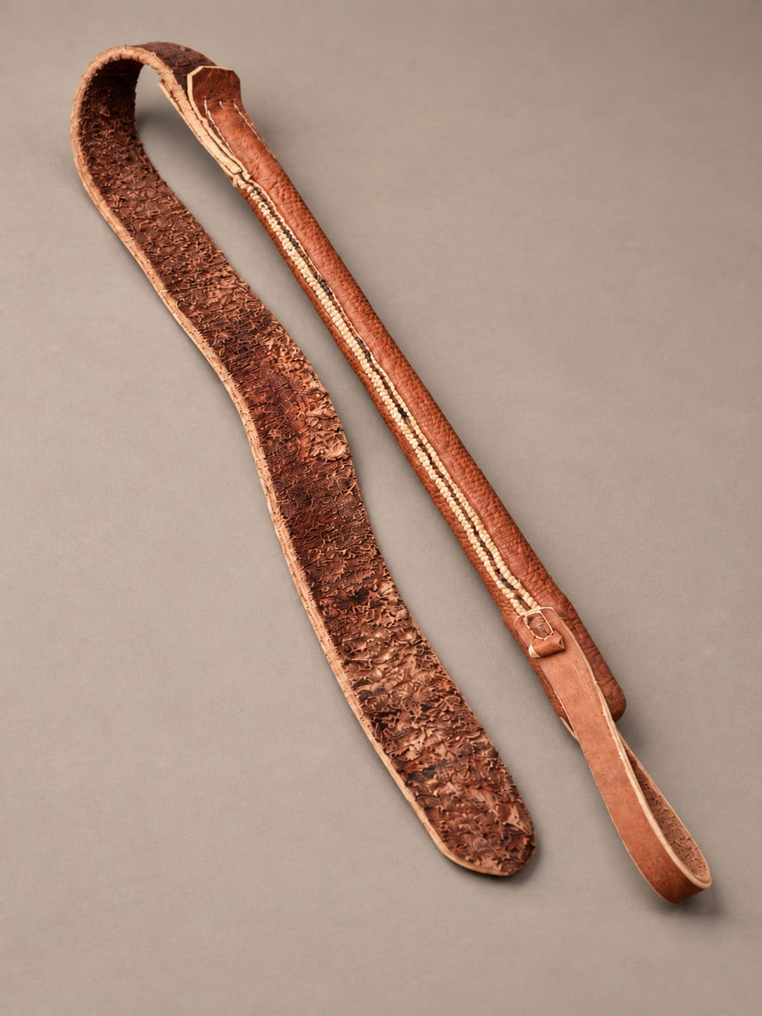 Argentine leather rebenque laid flat, showing the underside of its wide leather strap and the detailing along the handle.